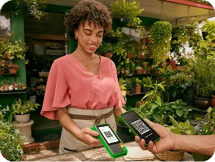 Empreendedora em frente ao seu estabelecimento físico, finalizando uma venda com a máquininha do Ton.