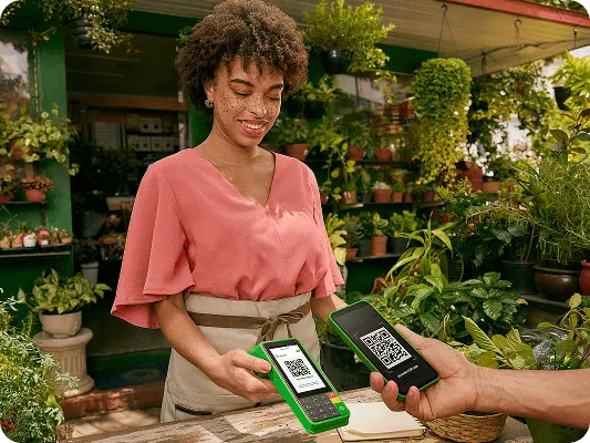 Empreendedora em frente ao seu estabelecimento físico, finalizando uma venda com a máquininha do Ton.