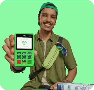 Empreendedor com um sorriso no rosto, mostrando o visor de sua maquininha verde com a logo do Ton