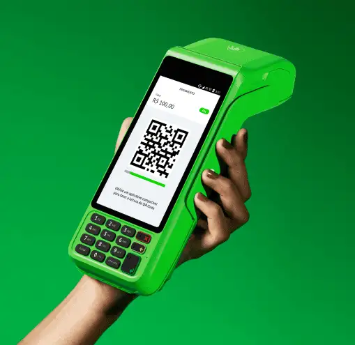 Em um fundo verde, uma mão de mulher segurando uma máquina de cartão do Ton com o valor de R$100 no visor, além do QR Code.